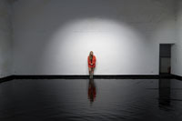 Installationskünstlerin Danuta Karsten in ihrer Wasser-Rauminstallation. Sie steht im Lichtkegel in einem leeren Raum, dessen Boden mit Wasser bedeckt ist.