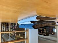 Auf einem Tisch liegen einige Akten, im Hintergrund stehen hinter einer Glasscheibe Bücherregale.