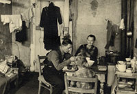Foto zeigt drei Personen, die in einem kleinen Zimmer am Tisch sitzen und essen.