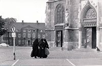 Foto zeigt einen großen Platz, den Domplatz von Münster. In der Mitte des Fotos sind drei Ordensfrauen zu sehen, die miteinander sprechen.