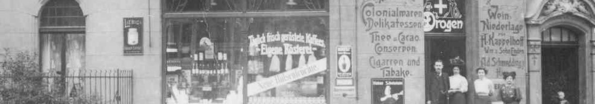 Altes Schwarzweiß-Foto eines Ladens mit Schaufenster und Tafeln, auf denen 'Tee,