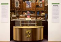 Werbung für koloniale Produkte: Dieser "Sarotti"-Pappaufsteller für Schokolade wurde in der Ausstellung "Aus Westfalen in die Südsee" des Stadtmuseums Münster 2018 gezeigt, arrangiert mit einer Anbiettheke aus dem Theater Münsters in den 1950er Jahren. Dahinter sind Ausstattungselemente des ehemaligen Kolonialwarenladens "Henke" aus dem Stadtmuseum zu sehen (Foto: Stadtmuseum Münster). Werbeaufsteller für Schokolade von "Sarotti" mit Ausstattungselementen eines alten Kolonialwarenladens in Münster (Foto: Stadtmuseum Münster).