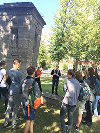 Eine Gruppe von Jugendlichen steht rund um das Traindenkmal, ein Obelisk aus Stein.