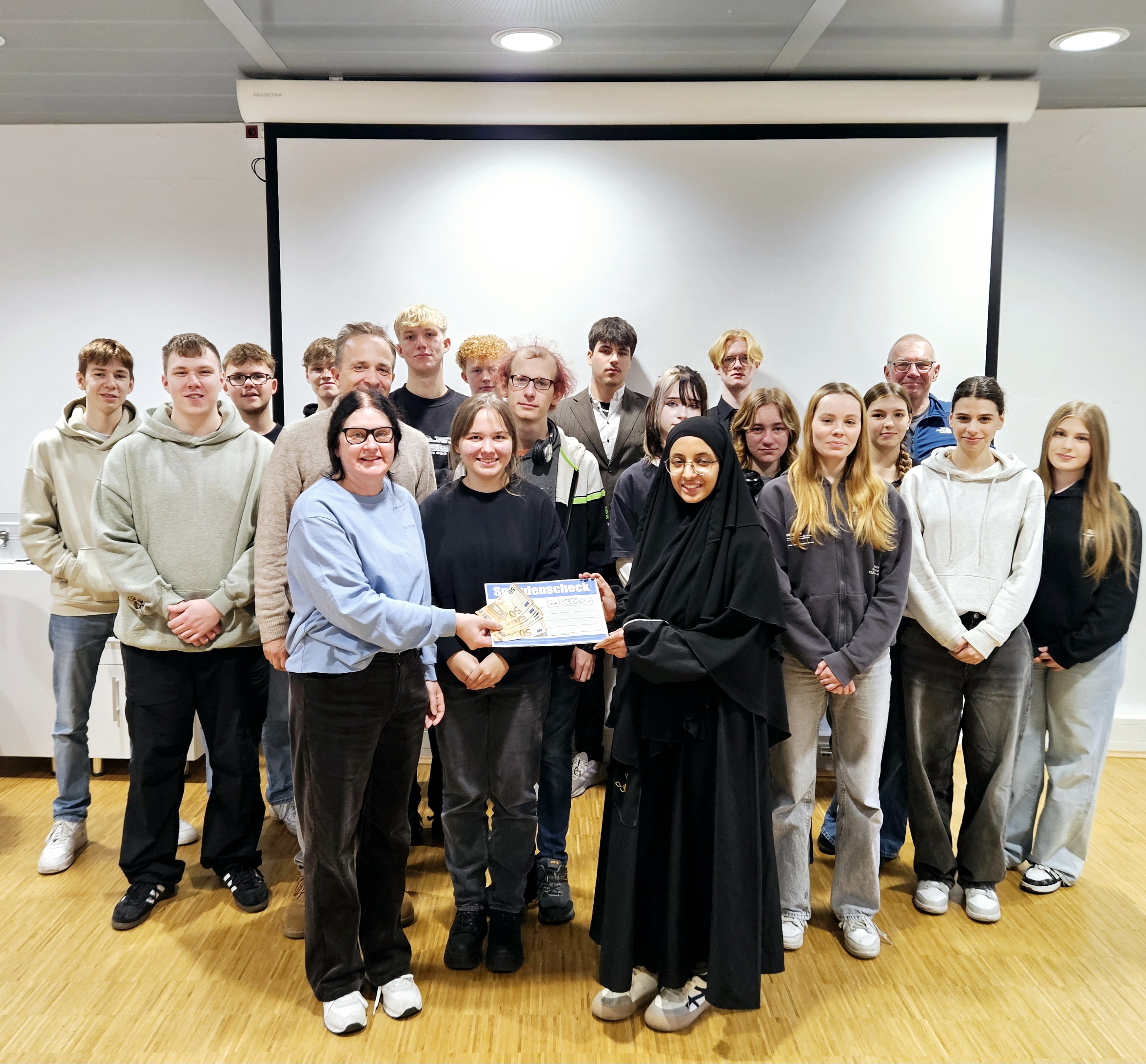 Gruppenbild der Schülerinnen und Schüler in einem hellen Raum, im Hintergrund eine leere Projektorleinwand.