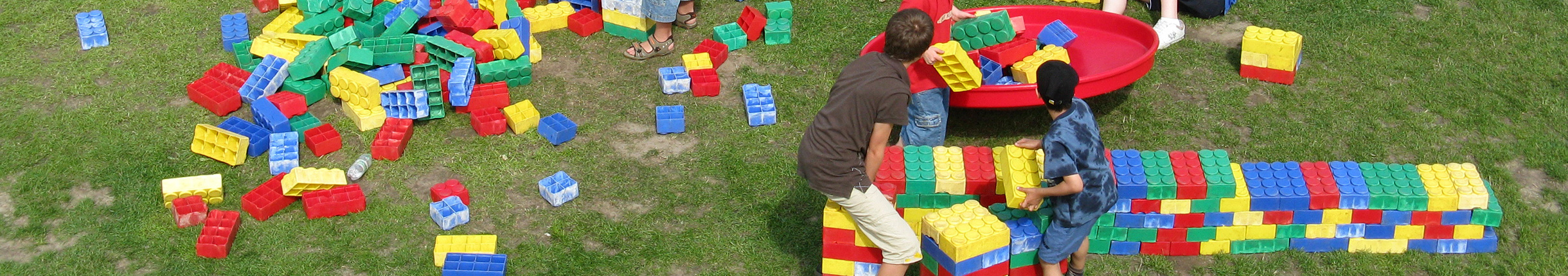 Kinder spielen mit großen Bausteinen auf einer grünen Wiese