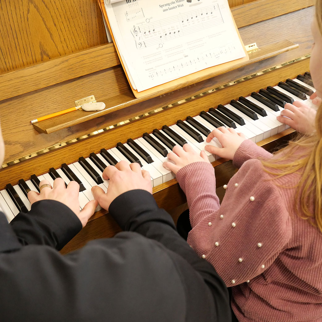 Ein Erwachsener und ein Kind spielen vierhändig Klavier.