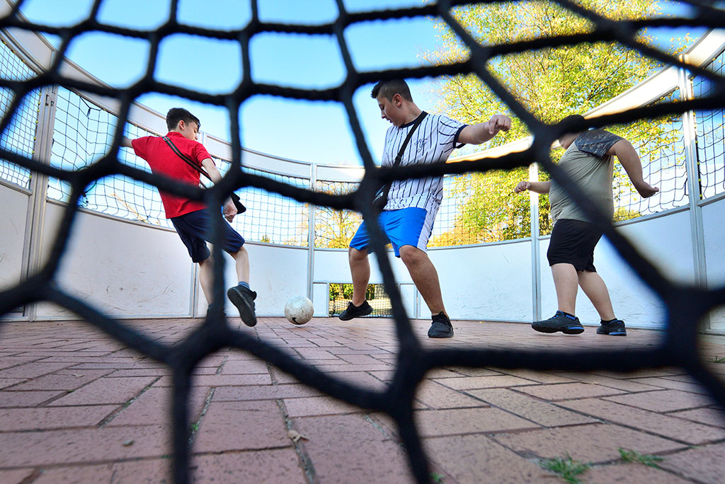 Drei Jugendliche spielen Fußball im Soccer-Cage