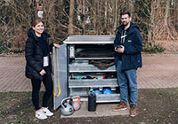 Zwei Personen stehen vor der geöffneten Sportbox und präsentieren den Inhalt.