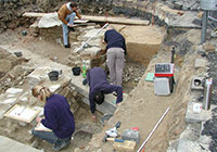 Drei junge Leute zeichnen und messen Fundstücke in einer Grabungsstelle.