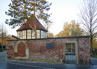 Rote Backsteinmauer mit Tor, dahinter ein Fachwerkbau