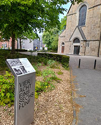 Infostele an einem Weg, im Hintergrund eine Kirche