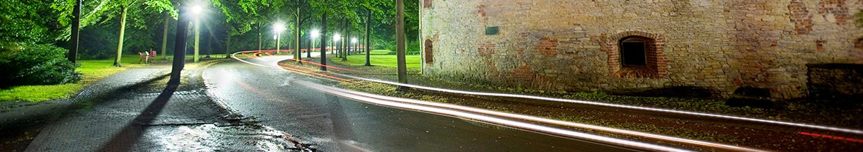 Leuchtende Streifen über nasser Straße vor einem Backsteingebäude