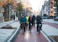 Das Foto zeigt eine große Gruppe Radfahrender mit lachenden Gesichtern, die den umgebauten Bohlweg entlangfahren.