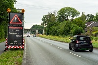 Auf dem Bild ist die Warendorfer Straße abgebildet, rechts auf dem Grünstreifen ist ein Hinweisschild aufgestellt, das digital anzeigt, dass hier in den Sommerferien, und zwar ab dem 13.07.2025, erfolgt. Auf der Fahrbahn sind fahrende Autos dargestellt