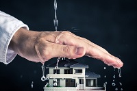 Starkregenschutz Eine schützende Hand wird über ein Haus gehalten, darüber fließt Wasser auf die Hand. Der Hintergrund ist schwarz.