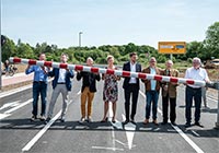 Gruppenfoto: Sieben Männer und eine Fraustehen auf einer Straße und halten eine Schranke.