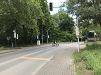 Blick auf die zweispurige Straße und die Ampelanlage mit der Rad- und Fußweg-Querung. Ein Fahrradfahrer überquert die Straße an der Ampelanlage.