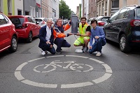 Vier Personen knieend auf einer Fahrradstraße und halten in der Mitte eine Ampel in der Hand.