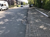 Sanierungsbedürftiger Asphalt auf der Straße, links im Bild steht ein weißer Bulli in der Parkbucht, rechts im Bild eine Busbucht.