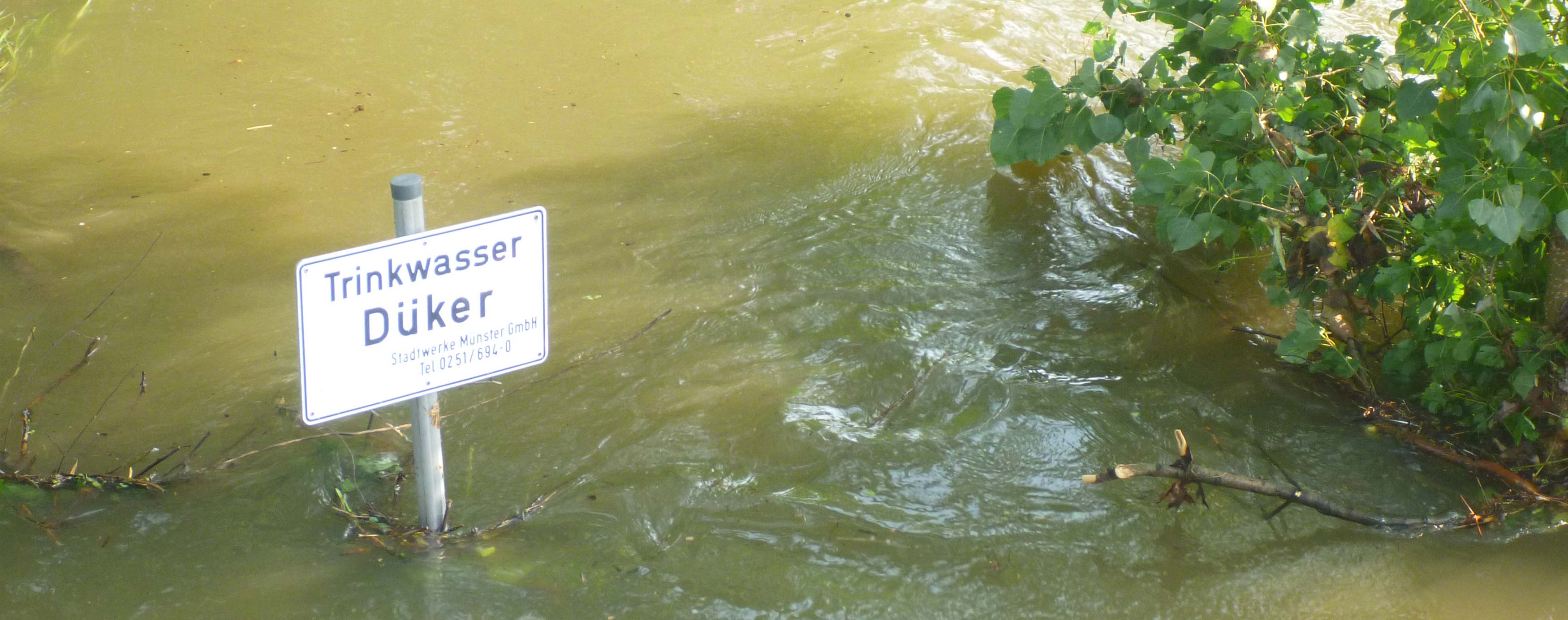 Ein Schild 'Trinkwasser-Düker' steht in braunem Wasser.