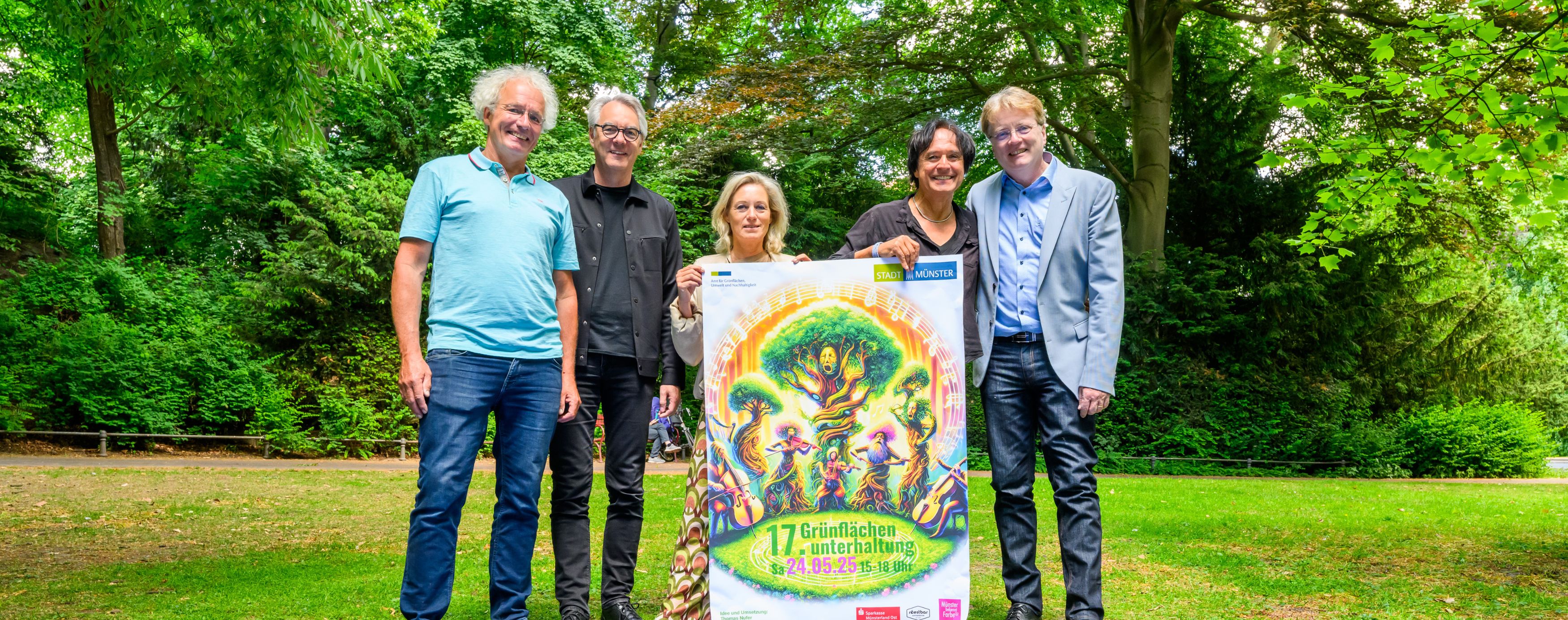Vier Personen stehen auf einer Wiese und präsentieren das Plakat für die Grünflächenunterhaltung 2025.