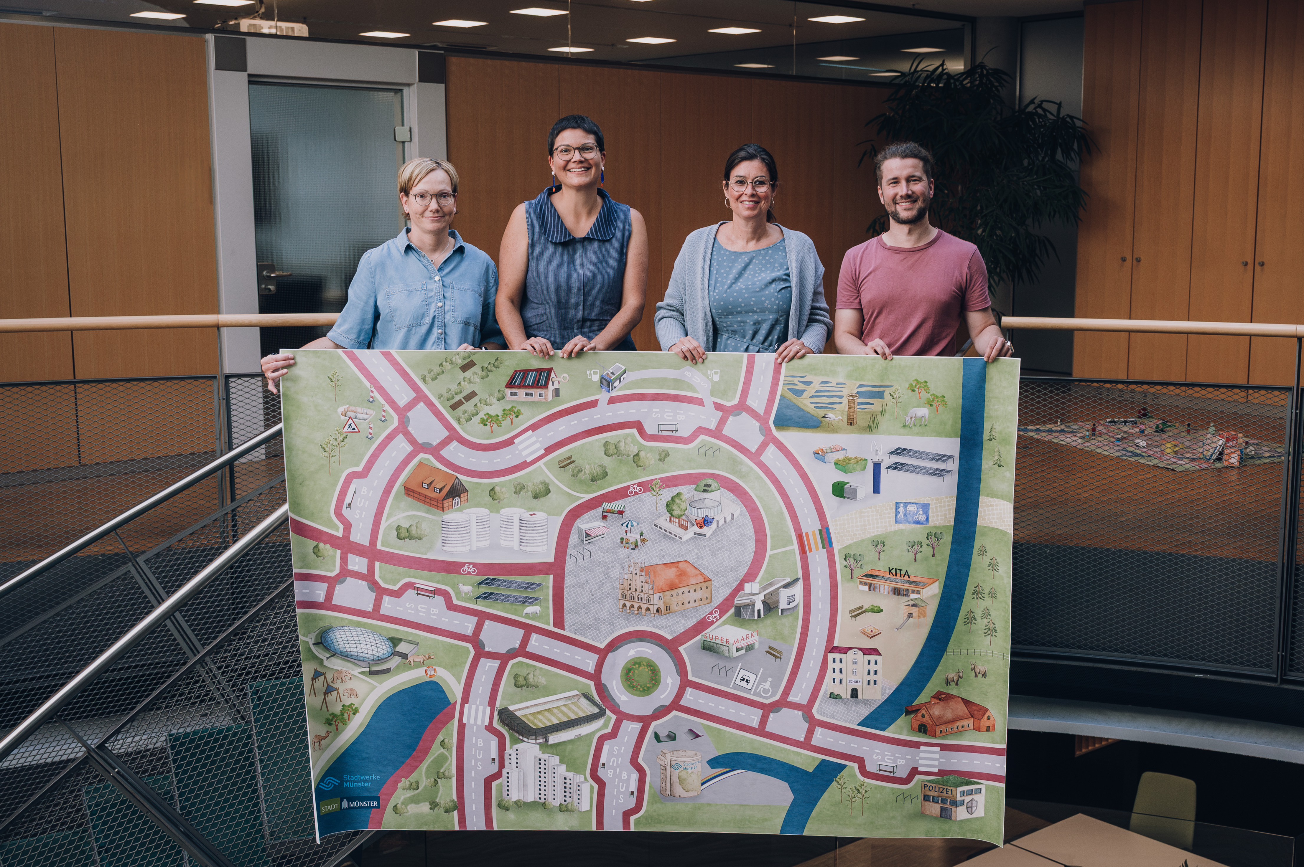 Vier Vertreter*innen der Stadt Münster präsentieren den neuen Münster-Spieleteppich.