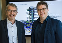 Helmut Heidrich und Vincent Linnemann vom Heidrich Ingenieurbüro GmbH stehen vor einer PowerPoint-Präsentation und lächeln in die Kamera.