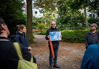 Klimadezernent Matthias Peck macht beim Klima-Spaziergang im Südviertel aufmerksam auf die Folgen des Klimawandels. Um ihn herum stehen die Teilnehmer:innen des Spaziergangs und hören zu.