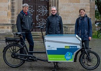 Klimadezernent Matthias Peck (Mitte), Veit Muddemann und Isabel Scherer von der Koordinierungsstelle für Klima und Energie (KLENKO) stehen hinter dem Lastenrad der KLENKO und lächeln in die Kamera.