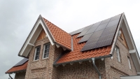 Auf dem Spitzdach eines Backsteinhauses sind mehre Photovoltaik-Module montiert.