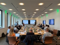 Workshop von Münsters Allianz für Klimaschutz in den Räumlichkeiten der Ratiodata SE, Foto: Gertec GmbH Bei einem Workshop von Münsters Allianz für Klimaschutz halten eine Frau und ein Mann gemeinsam eine Präsentation. An zwei langen Tischen sitzen die Workshop-Teilnehmenden.