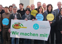 Teilnehmerinnen und Teilnehmer von Ökoprofit Münster halten den Schriftzug 'Wir machen mit!' in die Kamera.