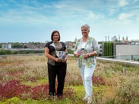Tatjana Kainz (l.) und Anna Castro Balbi vom Amt für Wohnungswesen und Quartiersentwicklung stehen auf einem Gründach und präsentieren Info-Broschüren.