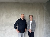 Christina Willerding und Wolfgang Nietan stehen vor einer Betonwand und lächeln in die Kamera.