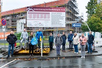 Menschengruppe steht vor einer Baustelle und lächelt in die Kamera.