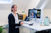 Ramona Leusch von der KLENKO vor einem PC-Bildschirm mit geöffneter Online-Konferenz lächelt in die Kamera