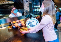 Eine junge Frau reicht einer Mitarbeiterin in der Gastronomie ein Glasgefäß über die Theke.