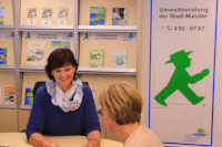 Beratung im Umweltbüro Eine Frau sitz mit einer anderen Frau an einem Tisch, hinter ihr Regale mit Broschüren.