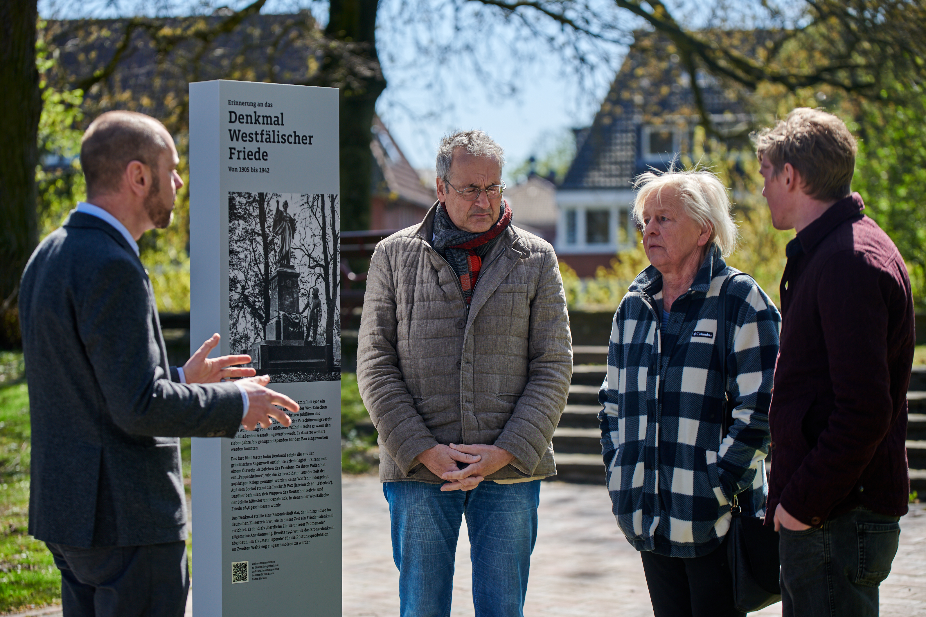 Dr. Peter Worm (l.) und Phillip Erdmann (r.) vom Stadtarchiv Münster präsentieren gemeinsam mit Bezirksbürgermeister Stephan Nonhoff und Marita Otte, Mitglied aus der Bezirksvertretung Mitte, die neue Info-Stele zum ehemaligen Friedensdenkmal.