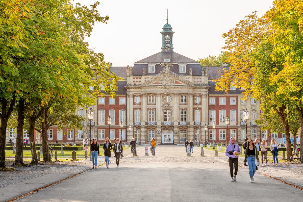 Blick auf den Haupteingang vom Schloss Münster mit vorbeigehenden jungen Menschen.