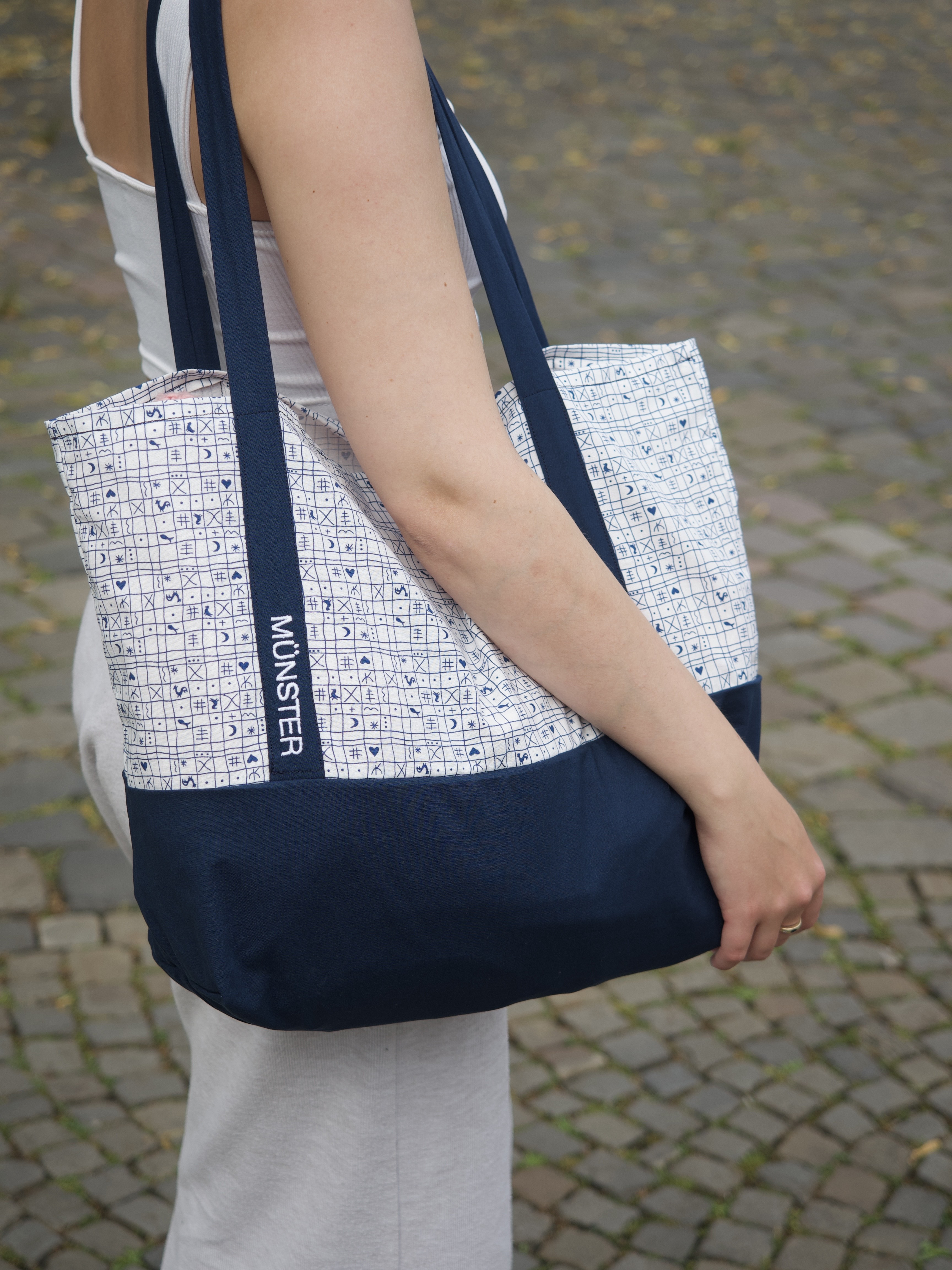 Eine Frau trägt eine Einkaufstasche mit der Aufschrift "Münster" über der Schulter.