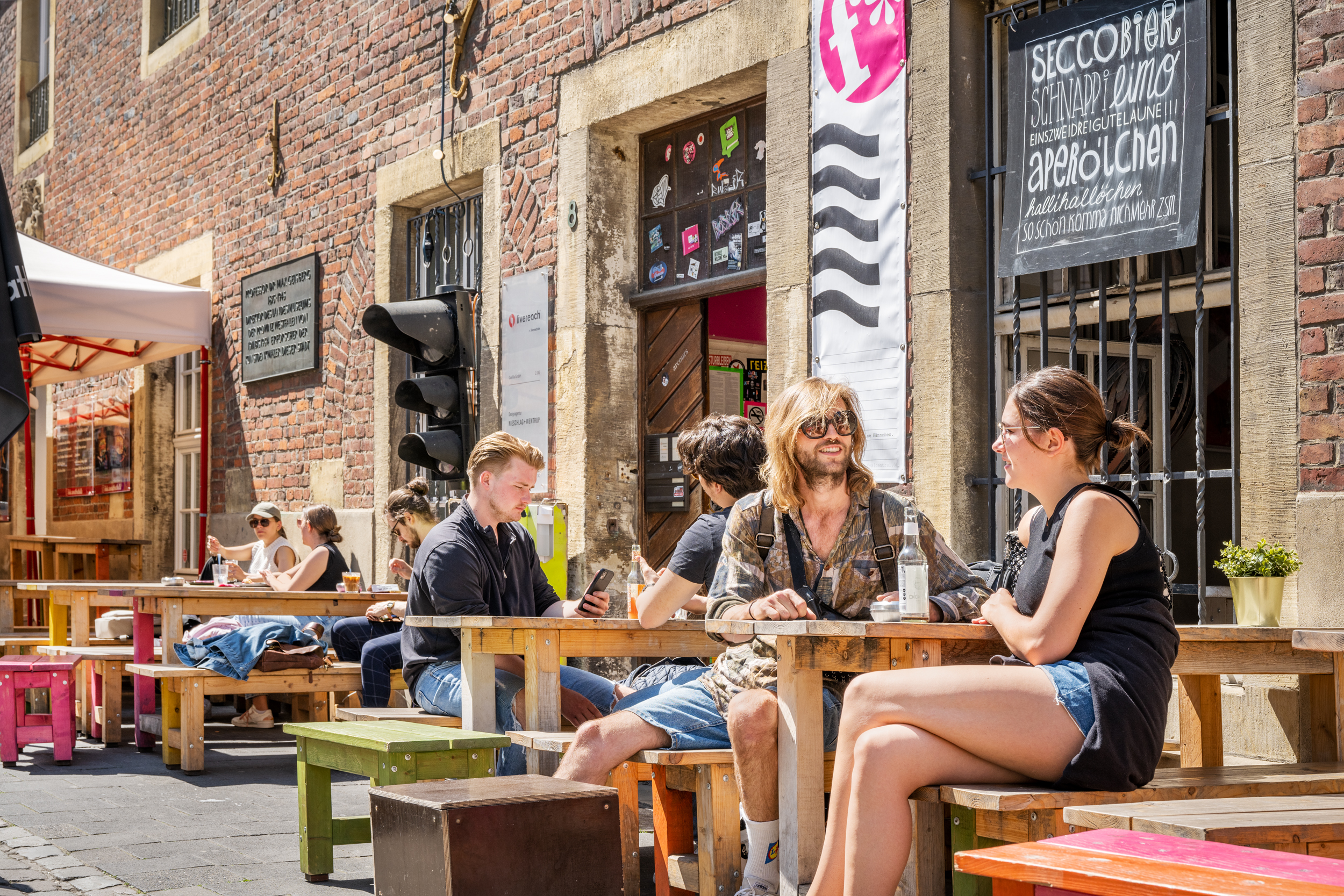 Junge Menschen sitzen bei Sommerwetter draußen vor einer Bar