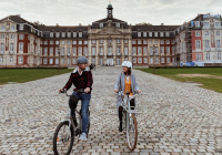 Eine Fahrradfahrerin und ein Fahrradfahrer vor dem Schloss in Münster