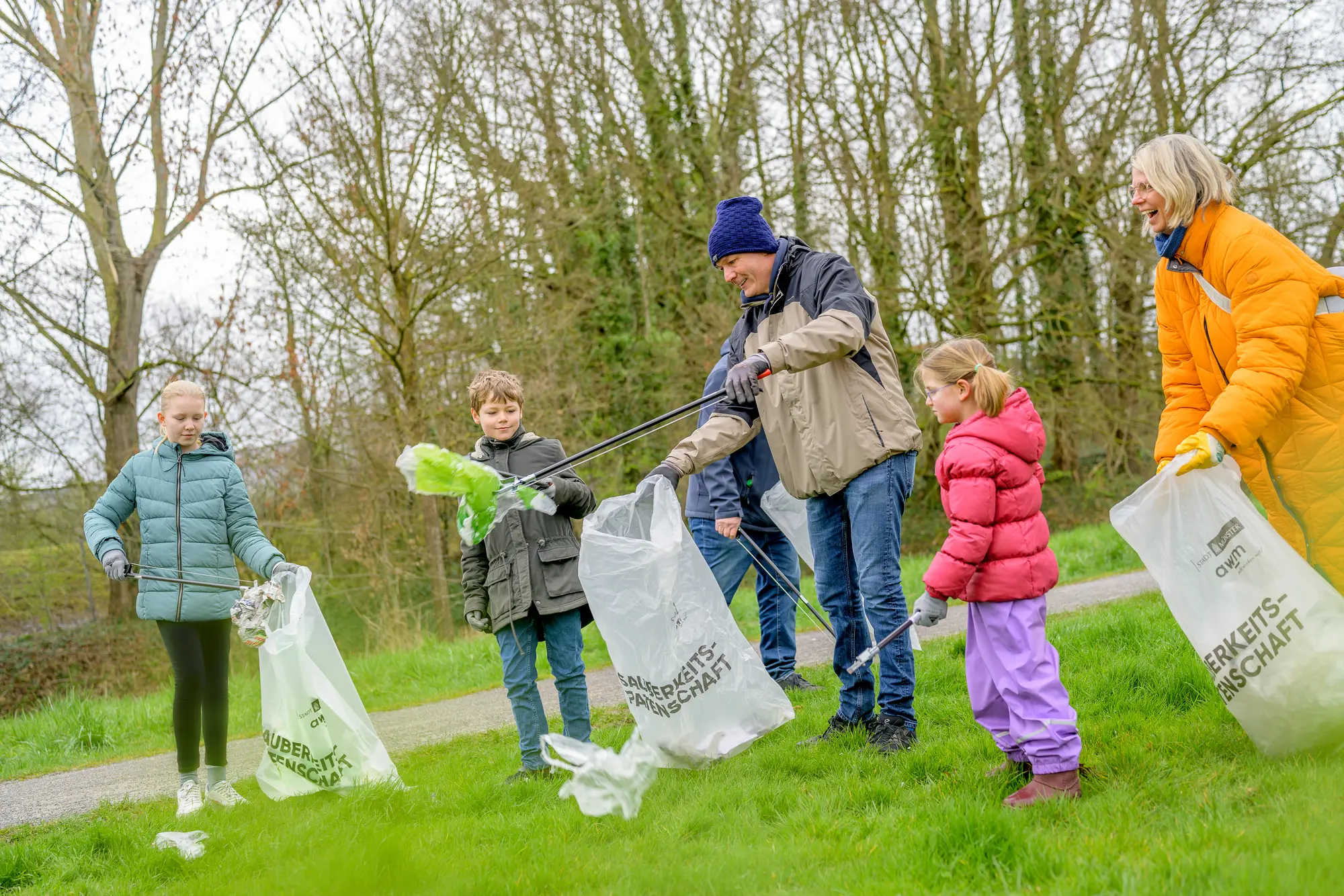 Das Bild zeigt 3 Erwachsende und 3 Kinder beim Abfallsammeln in einer Grünanlage