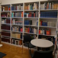 Blick in einen hellen Raum mit zwei Regalwänden, die voller Bücher sind, davor eine Sitzgruppe mit zwei Stühlen