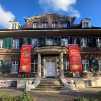 An der Fassade der Villa ten Hompel hängen vom ersten Stock zwei rote Banner bis zum Erdgeschoss hinab, auf dem "Gewalt gegen Frauen STOP. Violence against Women. Orange the World" steht.