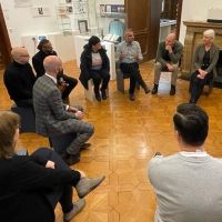 Polizist*innen aus Rishon Le Zion sitzen in einem Sitzkreis in einem Raum der Ausstellung der Villa ten Hompel und sprechen mit Peter Römer und Thomas Köhler.