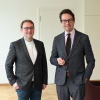 Andreas Bothe und Stefan Querl stehen in einem Büro nebeneinander und lächeln in die Kamera