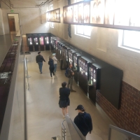 Menschen gehen durch einen hohen Raum, an dessen Wand viele Ausstellungstafeln hängen.