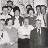 Ein Gruppenbild einer Familie mit insgesamt zwölf Personen, einige sitzend, andere stehend. Einige von ihnen lächeln, andere blicken ernst in die Kamera.